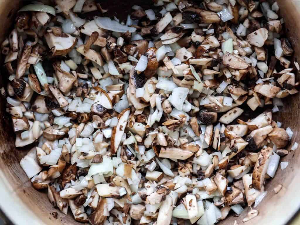 Chopped mushrooms and onions mixed together in a pot, ready to be cooked.